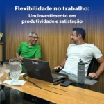 Dois homens em uma sala conversando de maneira descontraída, na frente deles há uma mesa com notebook e outros acessórios.